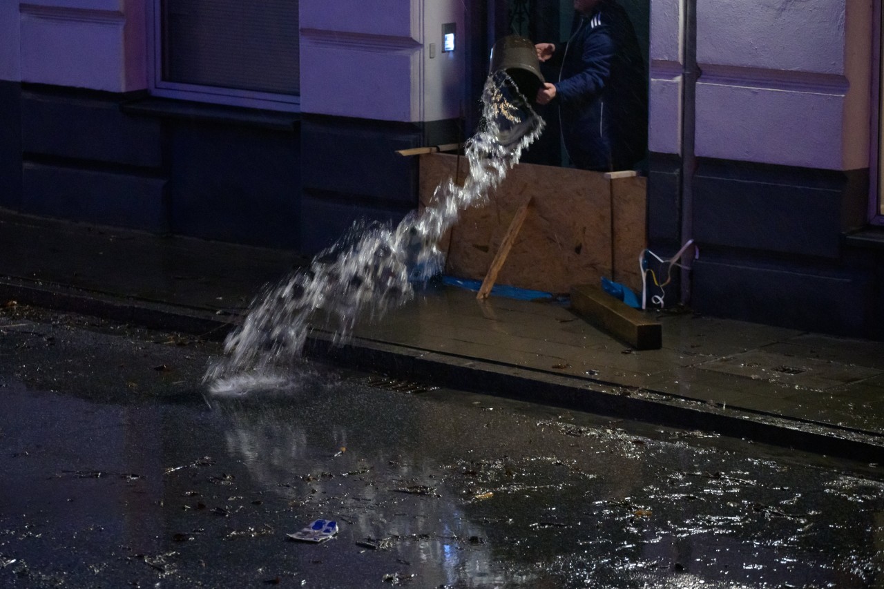 Ein Mann schüttet am frühen Morgen Wasser aus einem zuvor überfluteten Hauseingang in Hamburg.