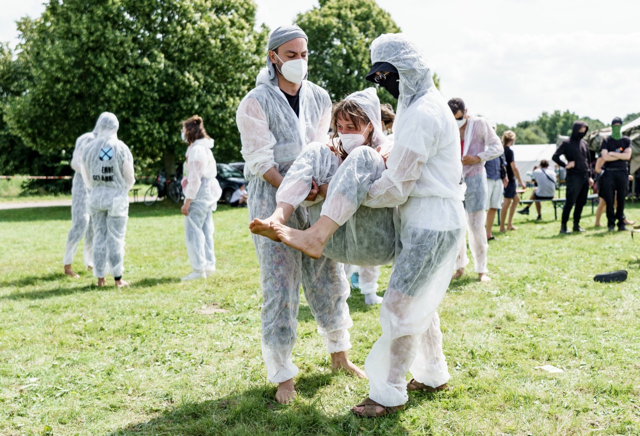 Klimaaktivisten in Schutzanzügen trainieren Verhalten bei Polizeimaßnahmen auf der Wiese eines Zeltcamps in Brunsbüttel.