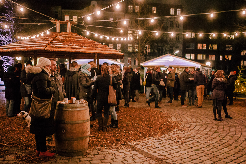 Menschen stehen an kleinen Ständen auf dem Weihnachtsmarkt.